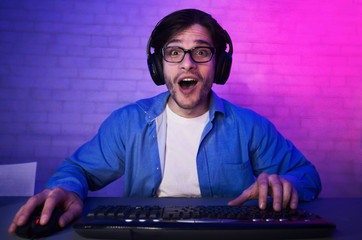 Surprised man playing online computer game, wearing headset