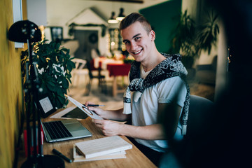 Cheerful freelance young handsome man checking statistical analyze while using laptop sitting in workspace at home