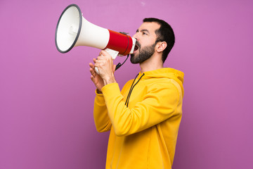 Handsome man with yellow sweatshirt shouting through a megaphone