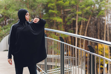 Hijab girl exercising on walkway bridge in early morning. Muslim woman wearing sports clothes doing stretching workout outdoors.