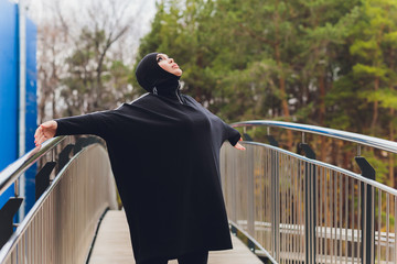 Hijab girl exercising on walkway bridge in early morning. Muslim woman wearing sports clothes doing stretching workout outdoors.