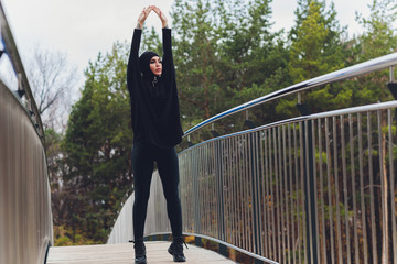 Hijab girl exercising on walkway bridge in early morning. Muslim woman wearing sports clothes doing stretching workout outdoors.