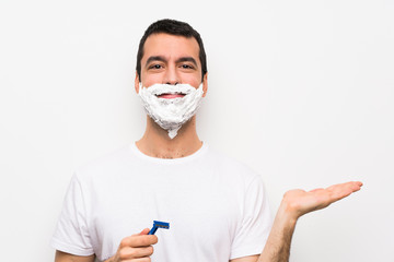 Man shaving his beard over isolated white background holding copyspace imaginary on the palm to insert an ad