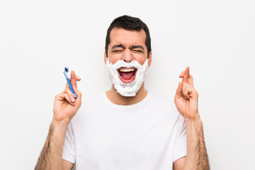 Man shaving his beard over isolated white background with fingers crossing