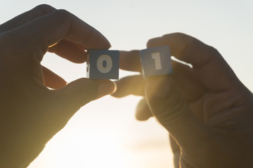 Man and women holds a Number zero and one in hands, sunset, sea background.