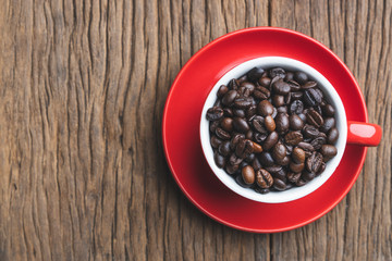 Topview of coffee beans in red cup  on old wooden table with copyspace.