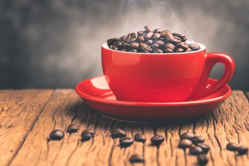 Coffee beans with smoke in red cup  on old wooden table with copyspace.