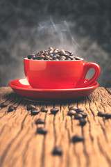 Coffee beans with smoke in red cup  on old wooden table with copyspace.
