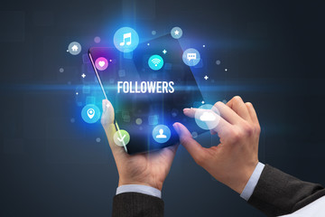 Businessman holding a foldable smartphone with FOLLOWERS inscription, social media concept