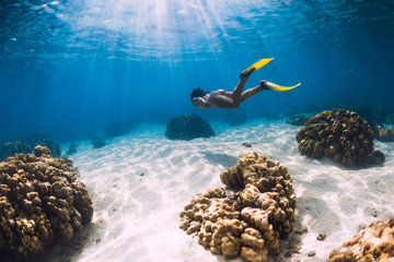 Free diver young girl with yellow fins glides over sandy bottom and corals.