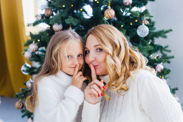 A girl with her mother near the Christmas tree, the interior decorated for the new year and Christmas, family and joy, traditions