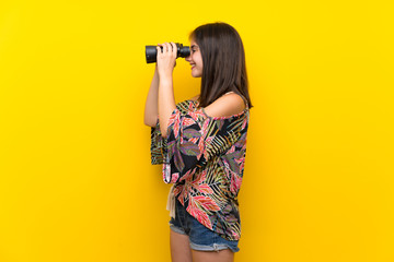 Caucasian girl in colorful dress over isolated yellow background with black binoculars