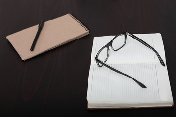 Glasses and a notebook lie on the dark table. The view from the top. Out of focus.