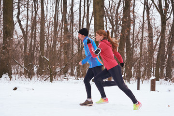 Happy smiling caucasian couple in sportswear running in nature. Winter time.