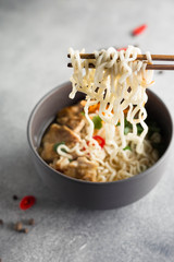 Spicy Asian noodles with chicken on chopsticks on a gray background. Image with a vertical orientation.