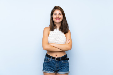 Young woman over isolated blue background keeping the arms crossed in frontal position