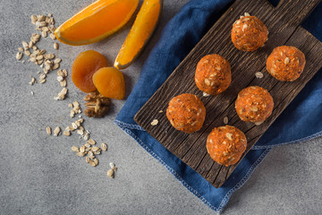 Energy balls from walnuts, dried apricots, orange and oatmeal on a wooden board and on blue textile on a dark gray background. Top view image