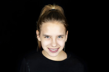 Fototapeta premium Beautiful young girl is sincerely smiling on a dark background, she has a beautiful smile because she wore braces on her teeth