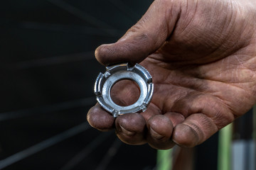 Repair bicycle wheel. Spoke key in the mechanic's hand. Rear wheel of a mountain bike on a black background. Dirty hands and fingers of a worker.