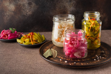 Homemade fermented cabbage, zucchini and carrots in jars on a dark ceramic plate on a brown background. Image with horizontal orientation, copy space