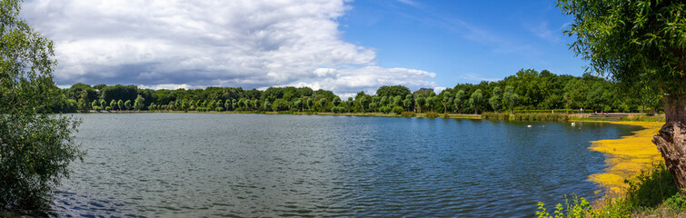 Fototapeta na wymiar Panoramic view over the lake in the public park Pildammsparken in Malmö, Sweden, during a summer day when clouds are building up on the horizon