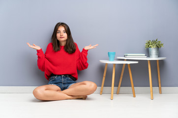 Young woman sitting on the floor having doubts with confuse face expression