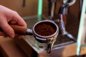 A portrait of a barista holding a coffee portafilter with fresh coffee grounds in it ready to make some coffee in the coffee machine.