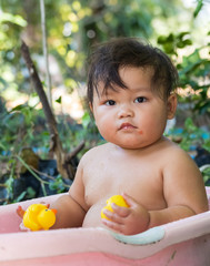 Adorable Asian baby girl having bath in pink tub on nature background.