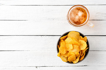 Overhead shot of glass of beer and potato chips in bowl on wooden table