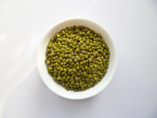 Mung bean (Vigna radiata) seeds in white bowl isolated on white background. Flat lay (top view). Dried raw mung seeds, pile of green beans in cup, Mung dal.