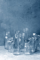 Variety of different shape empty opened glass bottles with and without lids standing on grey table with wall as background. Color of the year 2020 classic blue toned