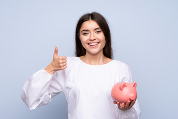 Young woman over isolated blue background holding a big piggybank