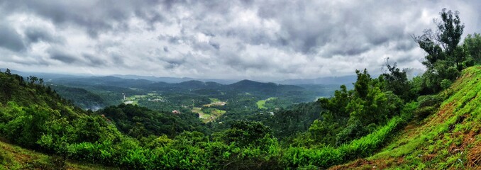 A landscape panorama of green hills with cloudy sky on the background in Coorg, India.
