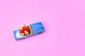 BLUE LIMOUSINE ON A PINK BACKGROUND WITH A BOX OF GIFT AND RED BOW. Miniature mini toy.