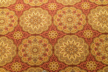 Close up of a detail or a fug or tapestry on the floor in yellow and orange and gold with circular...