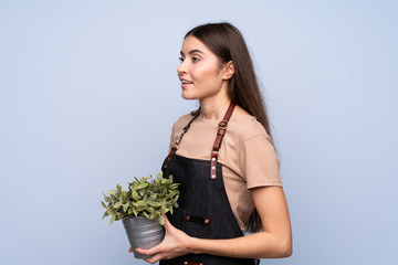 Young woman over isolated blue background taking a flowerpot