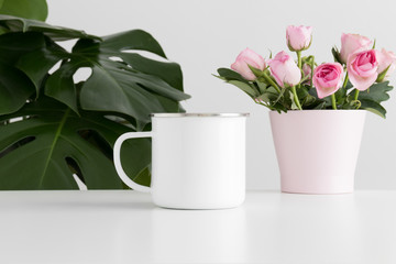 Enamel mug mockup with pink roses in a pot and a monstera plant.