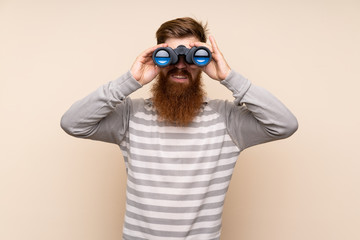 Redhead man with long beard over isolated background with black binoculars