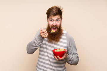 Redhead man with long beard over isolated background holding a bowl of cereals
