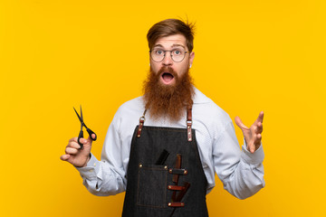 Barber with long beard in an apron over isolated yellow background with shocked facial expression