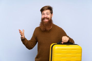 Redhead man with long beard holding a suitcase with shocked facial expression