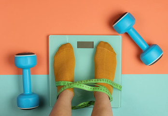 Fitness, slimming concept. Woman measures her weight by standing her feet in socks on scale against...