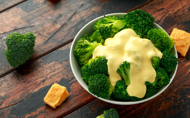 Broccoli with cheese sauce in white bowl on wooden table