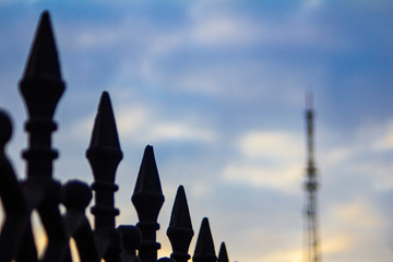 wrought iron fence against a blurred TV tower and barbed wire at sunset