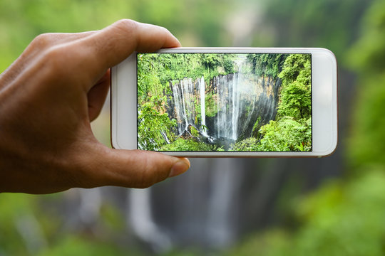 A tourist is taking pictures with a smartphone to the beautiful Tumpak Sewu Waterfalls. Tumpak Sewu Waterfalls are a tourist attraction in East Java, Indonesia.