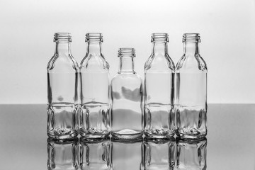 Monochrome glass bottles in backlight. Reflection of five bottles on a dark reflective background.