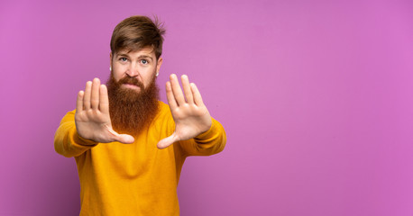 Redhead man with long beard over isolated purple background making stop gesture and disappointed