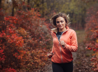 Jogging through the autumn forest. A young fit woman in sportswear runs along a forest path with reddened leaves. Healthy lifestyle concept