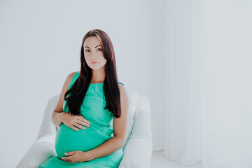 a pregnant woman before childbirth sits in white couch