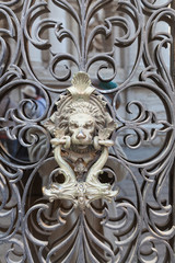 Fototapeta na wymiar Historic brass door knocker of a Lions Head and Serpents on ornate grille